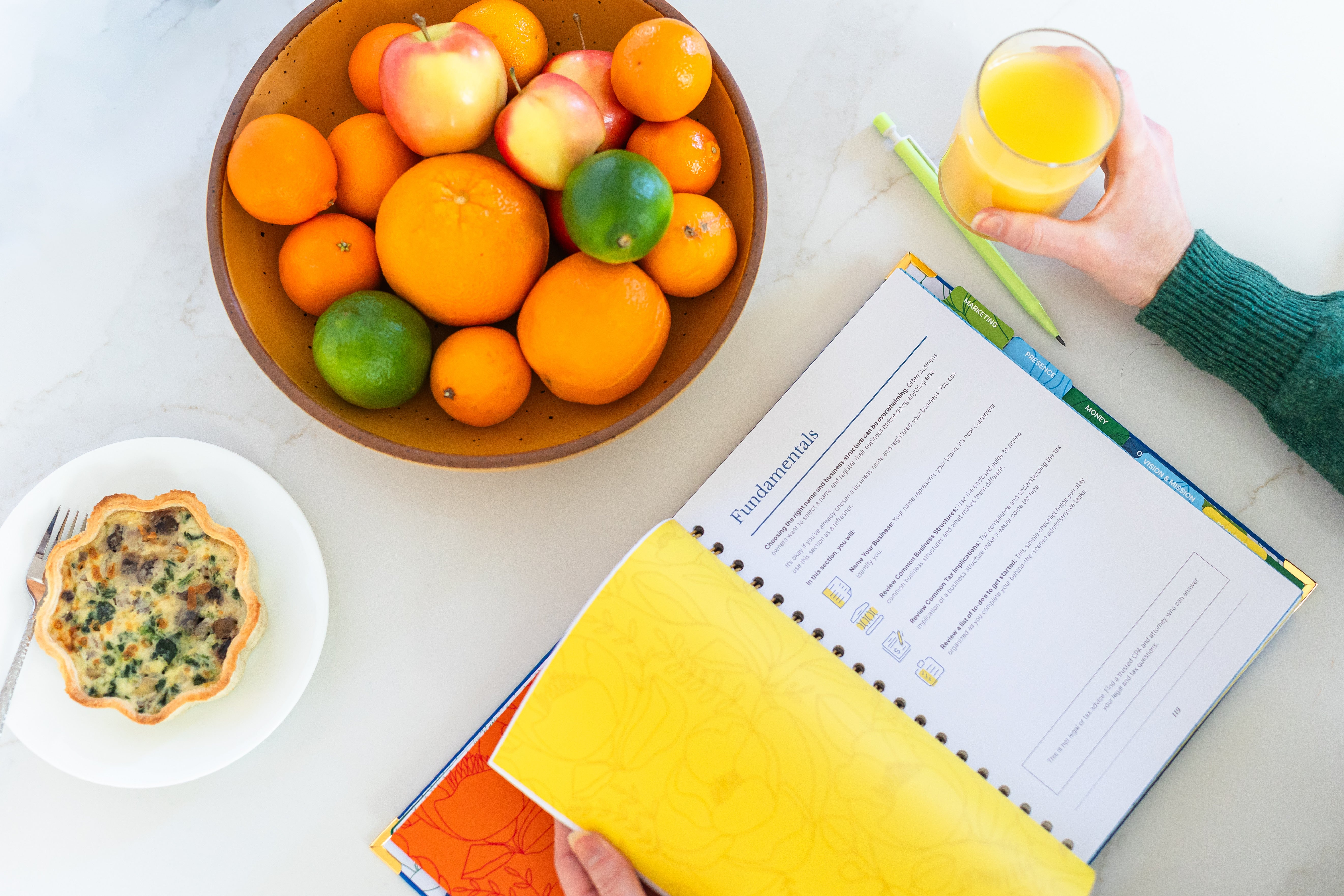 Picture of the Fundamentals chapter of The Guided Small Business Planner with a pencil, a hand holding a glass and some food.